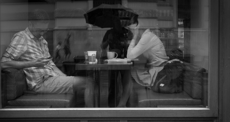 Two people sitting in a restaurant booth near the window, one lazily looking at their phone
