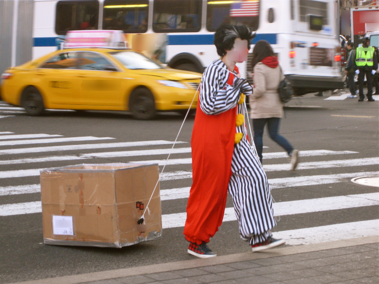 A clown dragging a box through a city crosswalk
