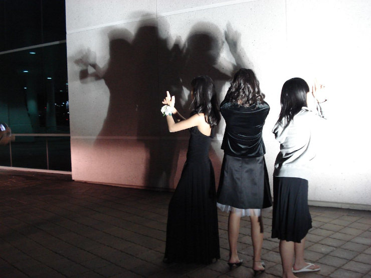 Three women attempting to strike the "Charlie's Angels" title card pose in silhouette