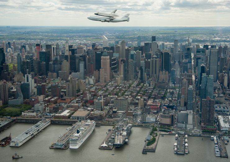 An aerial photograph showing Pier 86 with the Intrepid Museum at bottom center, and the Enterprise carried above