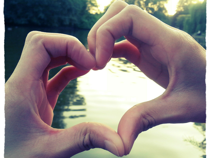 Fingers held in a heart shape in front of a body of water