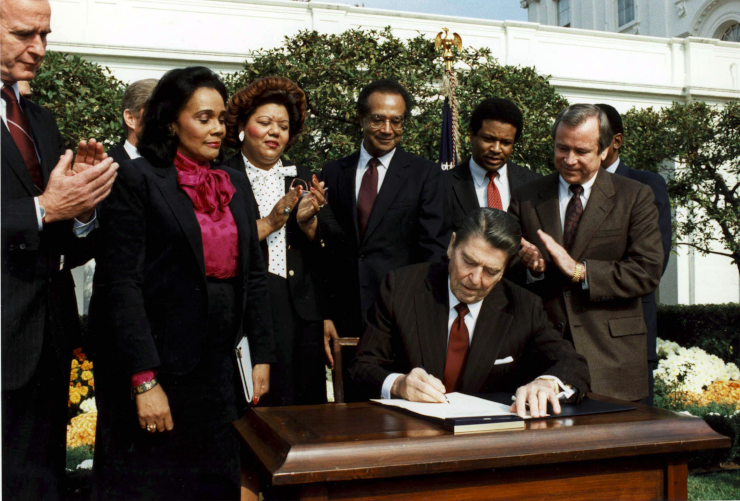 Ronald Reagan signing the bill creating the national holiday, reluctantly, by many reports
