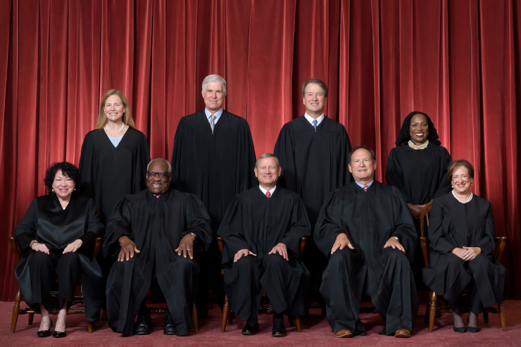 Formal group photograph of the Supreme Court as comprised on June 30, 2022, after Justice Ketanji Brown Jackson joined the Court. The Justices pose in front of red velvet drapes and arranged by seniority, with five seated and four standing.