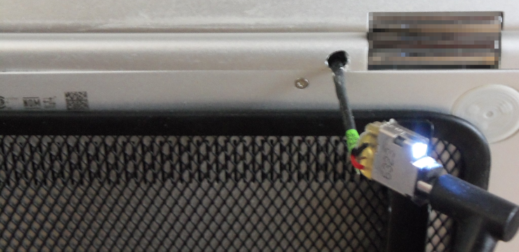 A hole drilled into the back of a laptop case, with a power cord dangling out